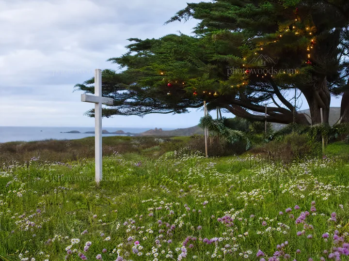 White Christian cross in wildflower meadow by the sea - AI-generated stock image
